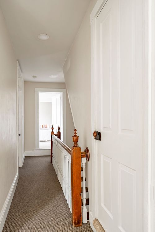 Narrow upstairs hallway with a dark wood stair railing and white paneled doors.