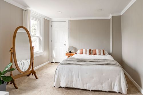 Bedroom with a paneled accent wall, full-length oval mirror and striped throw pillows.