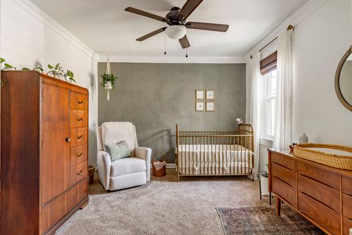 Nursery with a sage accent wall, wood spindle crib, glider chair and framed art prints.