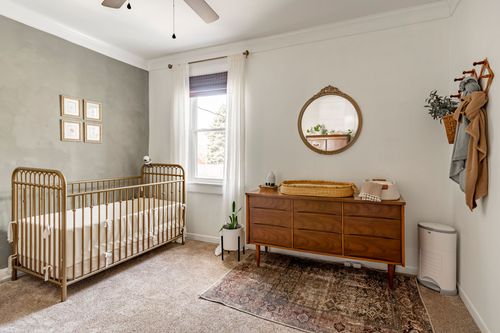 Nursery with a wood slat crib, round mirror over a mid-century dresser and a woven changing basket.