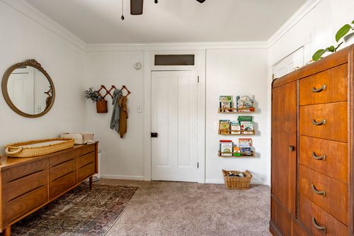 Room with a round wall mirror, mid-century dresser and a tall wood armoire in the corner.
