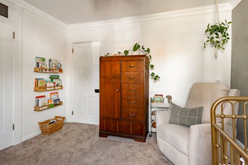 Kids room corner with a tall wood armoire, floating bookshelves and a cream glider chair.