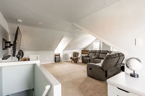 Attic bonus room with sloped ceilings, a gray reclining sectional and mounted TV.