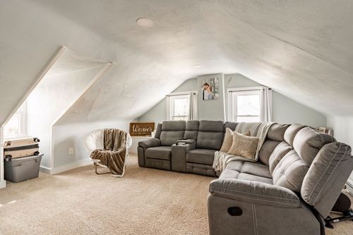 Vaulted bonus room with a gray reclining sectional, accent chair and dormer windows.