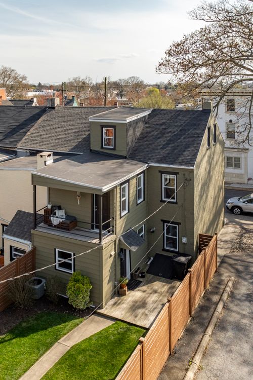 Aerial view of a renovated home with a rooftop balcony and wooden privacy fence