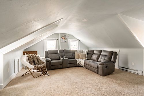 Bonus room with sloped ceiling, a gray sectional sofa and a woven accent chair with a throw.