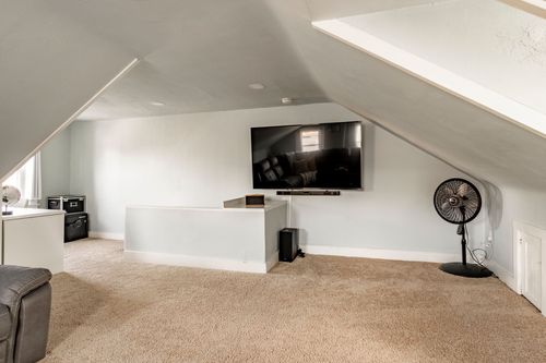 Attic media room with a wall-mounted TV, white console cabinet and portable fan.