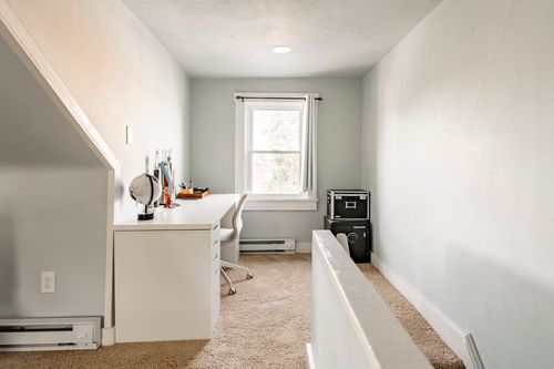Narrow attic office nook with a white built-in desk, task chair and a single window.