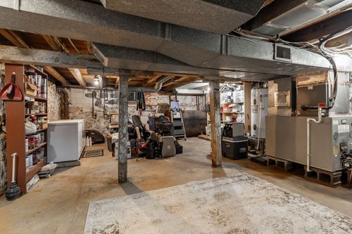 Unfinished basement storage area with wood shelving, stone walls and exposed ductwork.