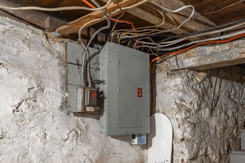 Basement electrical panel mounted on an old stone foundation wall with exposed wiring.