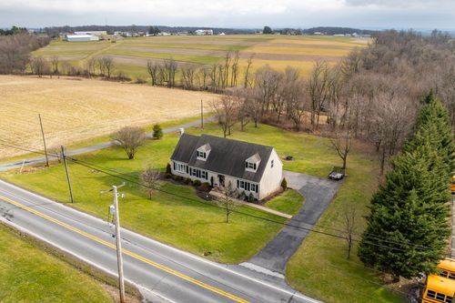 Aerial view of a cape-style farmhouse surrounded by open fields along a country road.