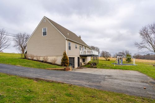 Rear elevation of a two-story home with a wraparound deck and mature shade tree.