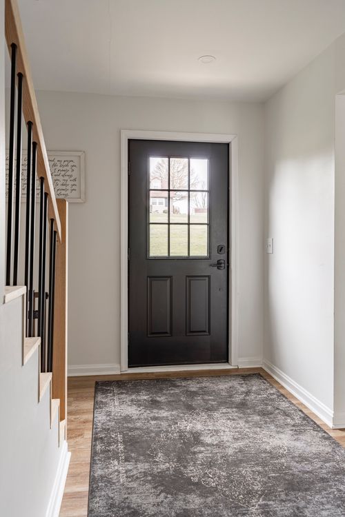 Entryway with a black paned front door, wood stair railing and a dark area rug.