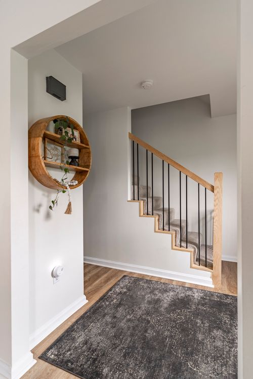 Entry landing with a round floating shelf, wood and black stair railing, and a patterned rug.