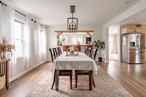 Bright dining room with a lantern chandelier, long wood table and sheer curtains.