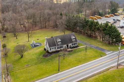 Aerial view of a cape-style home with a wooden swing set and mature shade trees in the yard.