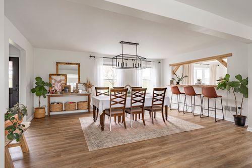 Dining room with a wood dining table, gilt mirror over a console, and leather barstools beyond.