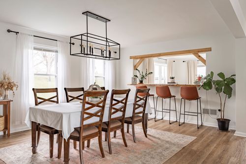 Dining room with a rectangular chandelier, wood table and a peek into a bar seating area.