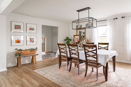 Dining room with a gallery wall, wood bench and a rectangular chandelier over the table.