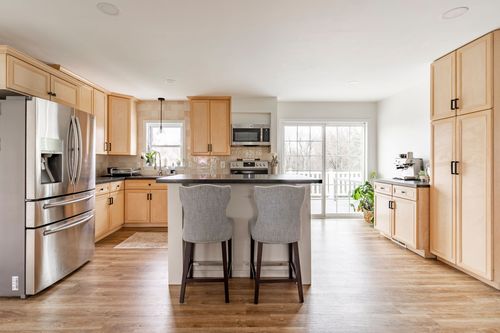 Kitchen with light wood cabinets, a stainless refrigerator, dark countertops and gray barstools.
