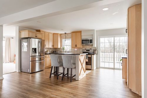 Open kitchen with light wood cabinetry, stainless appliances and a view to a rear deck.