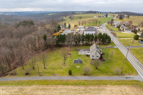 Aerial view of a cream two-story home surrounded by farmland, silos and evergreen trees.