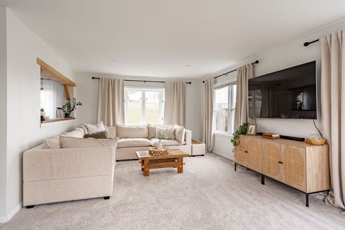 Living room with a cream sectional sofa, wood coffee table and wall-mounted TV over a cane console.