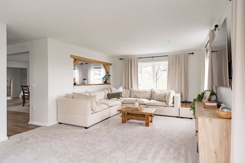 Open-concept living room with a beige sectional, wood coffee table and sightline into the kitchen.