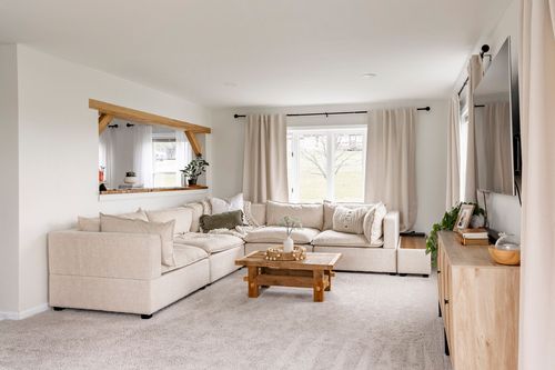 Living room with a plush beige sectional, wood coffee table and large front window.