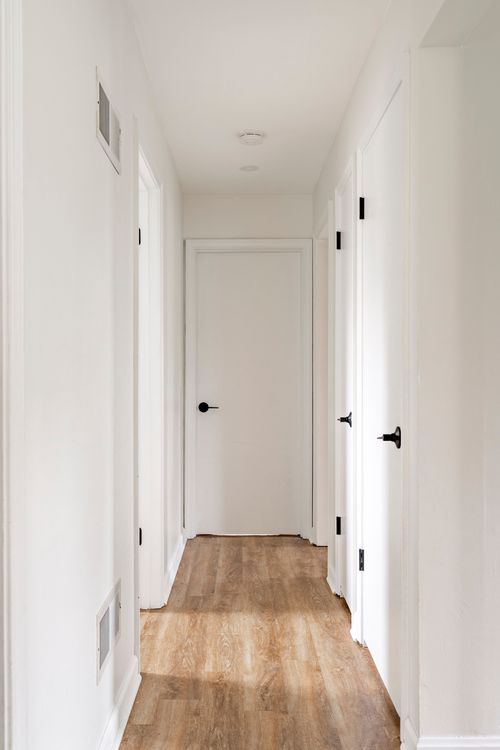 Straight hallway with white paneled doors and warm wood flooring.
