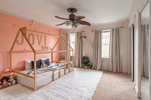 Kids bedroom with a coral accent wall, wood house-frame bed and a ceiling fan.