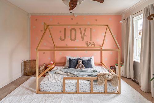 Kids bedroom with a coral polka-dot wall, wood canopy bed frame and personalized name decor.