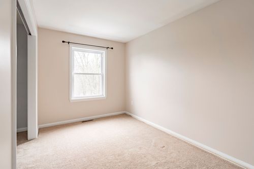 Empty bedroom with a single window, neutral walls and beige carpet.