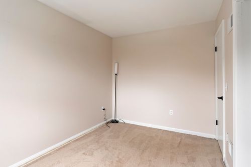 Empty bedroom corner with a floor lamp and wall-to-wall beige carpet.