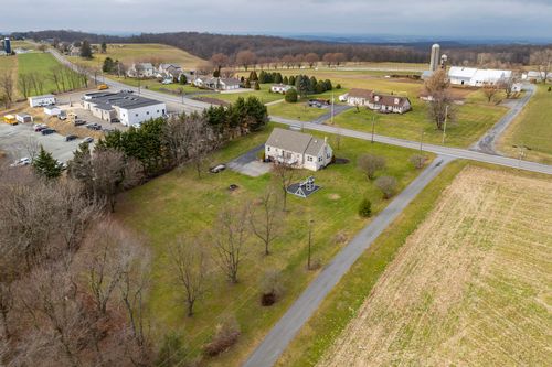 Aerial view of a cape-style home beside a country road, with grain silos and a storage building nearby.