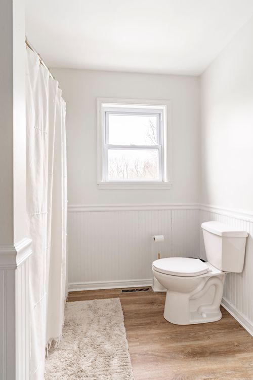 Bathroom with white wainscoting, a single window and a shag bath mat.