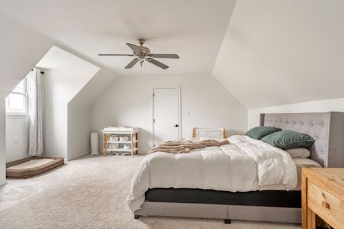Primary bedroom with a vaulted ceiling, ceiling fan and a gray tufted headboard.