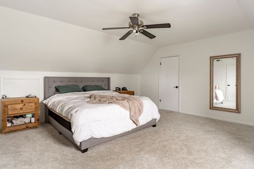 Bedroom with a gray tufted headboard, wood dresser and framed mirror.