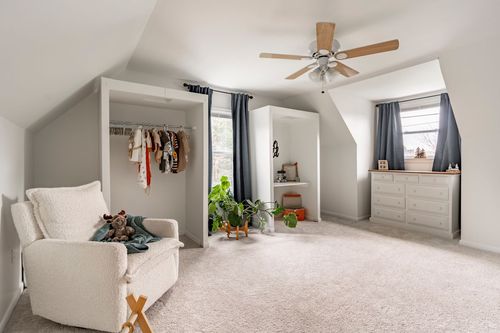 Bedroom with an open closet nook, cream armchair and hanging kids clothing.