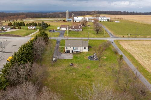 Aerial view of a cape-style home with mature trees and a grain silo visible across the road.