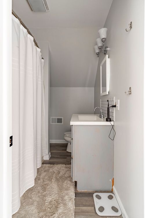 Attic bathroom with a distressed blue vanity, wall sconce and curtained shower.