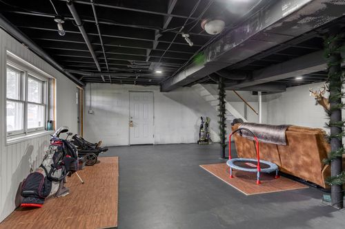 Basement rec room with golf bags, a mini trampoline and exposed ceiling joists.