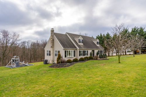 Aerial view of a cape-style home with a wood playset, evergreen trees and an asphalt driveway.