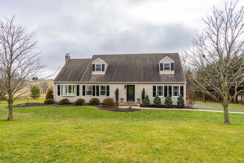 Cape-style home exterior with dormer windows, black shutters and a manicured front lawn.