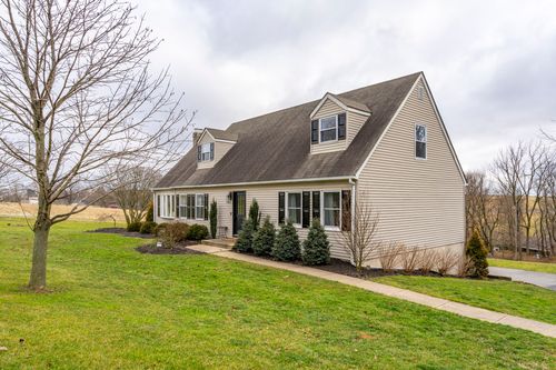 Side exterior of a cape-style home with a bay window, black shutters and an asphalt driveway.