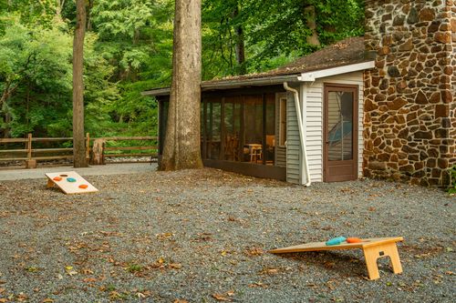 Screened porch addition with a stone chimney and cornhole boards set up on gravel.