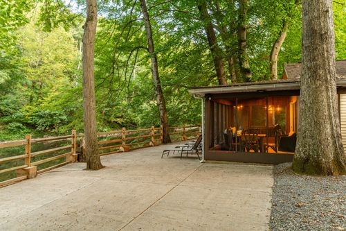 Concrete patio with a wood split-rail fence overlooking a wooded creek, screened porch glowing at dusk.