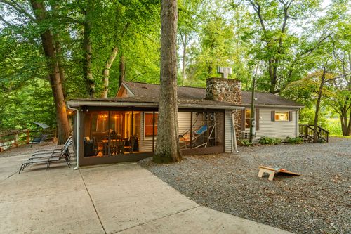 Cabin exterior at dusk with a glowing screened porch, stone chimney and lounge chairs on the patio.