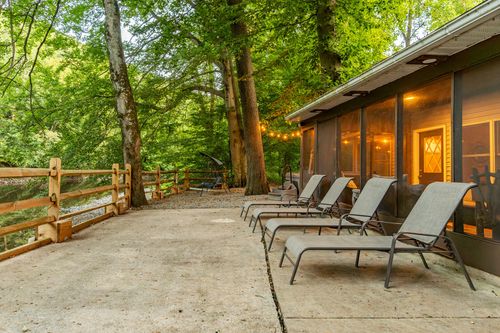 Patio lounge chairs lined up beside a lit screened porch and wood split-rail fence at dusk.