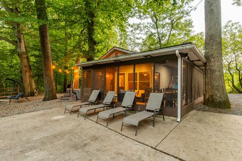 Cabin patio at dusk with lounge chairs, string lights and a glowing screened porch.